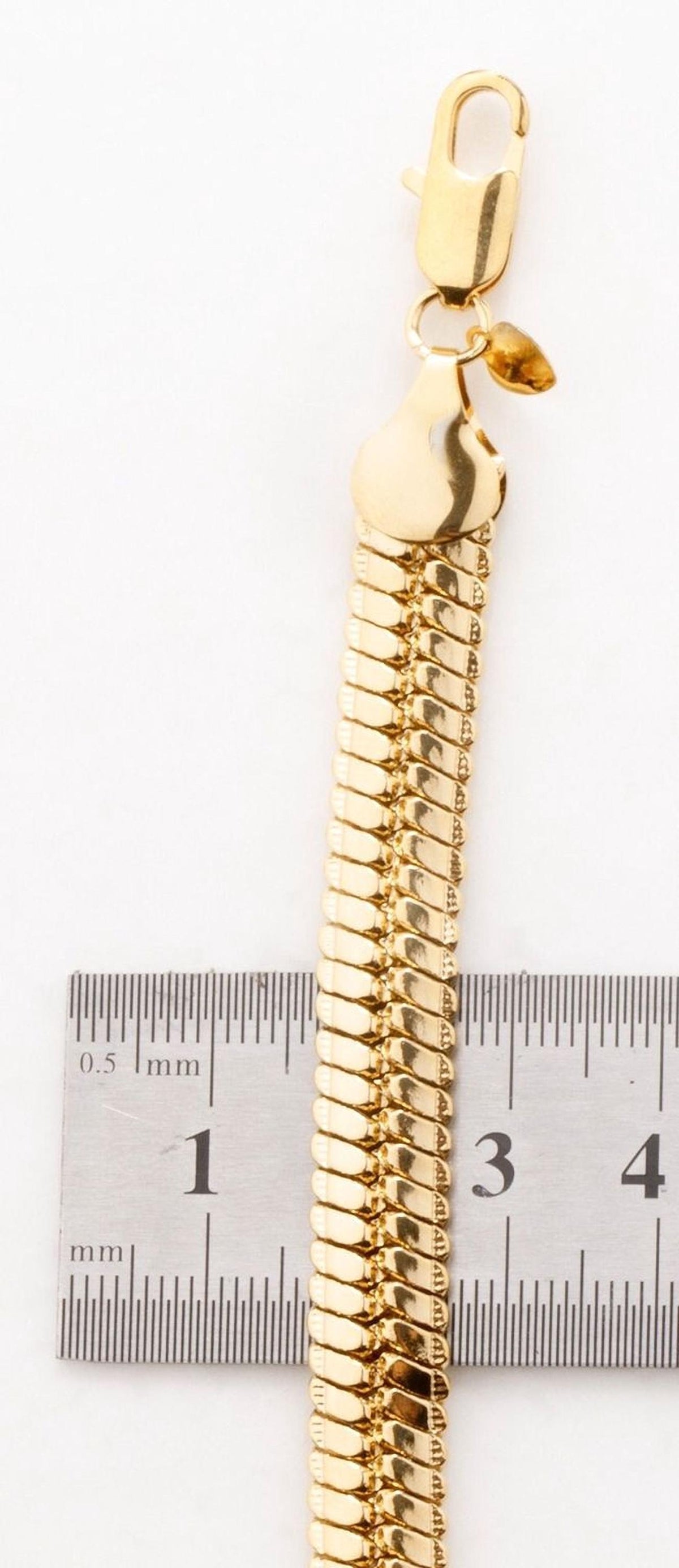A gold-colored bracelet with a clasp and a ruler for size comparison.