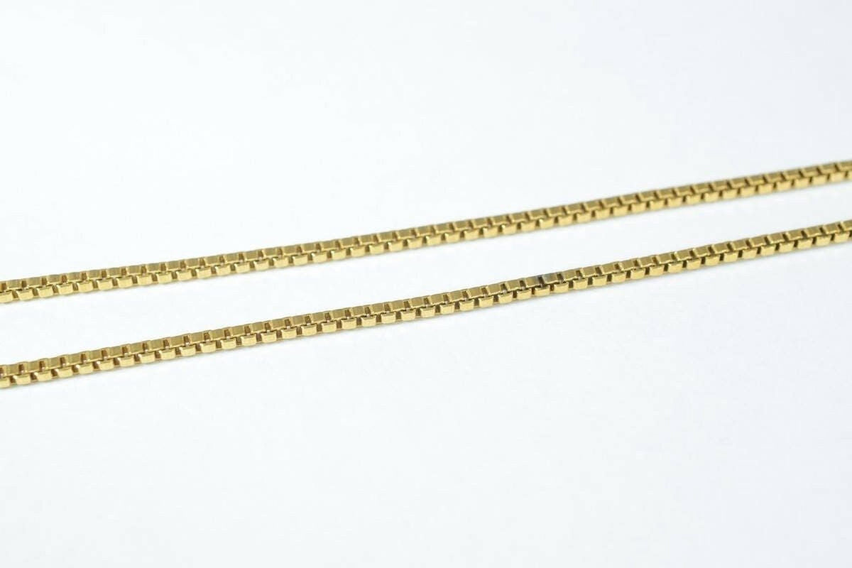 A close-up image of a gold-colored necklace chain with square links.