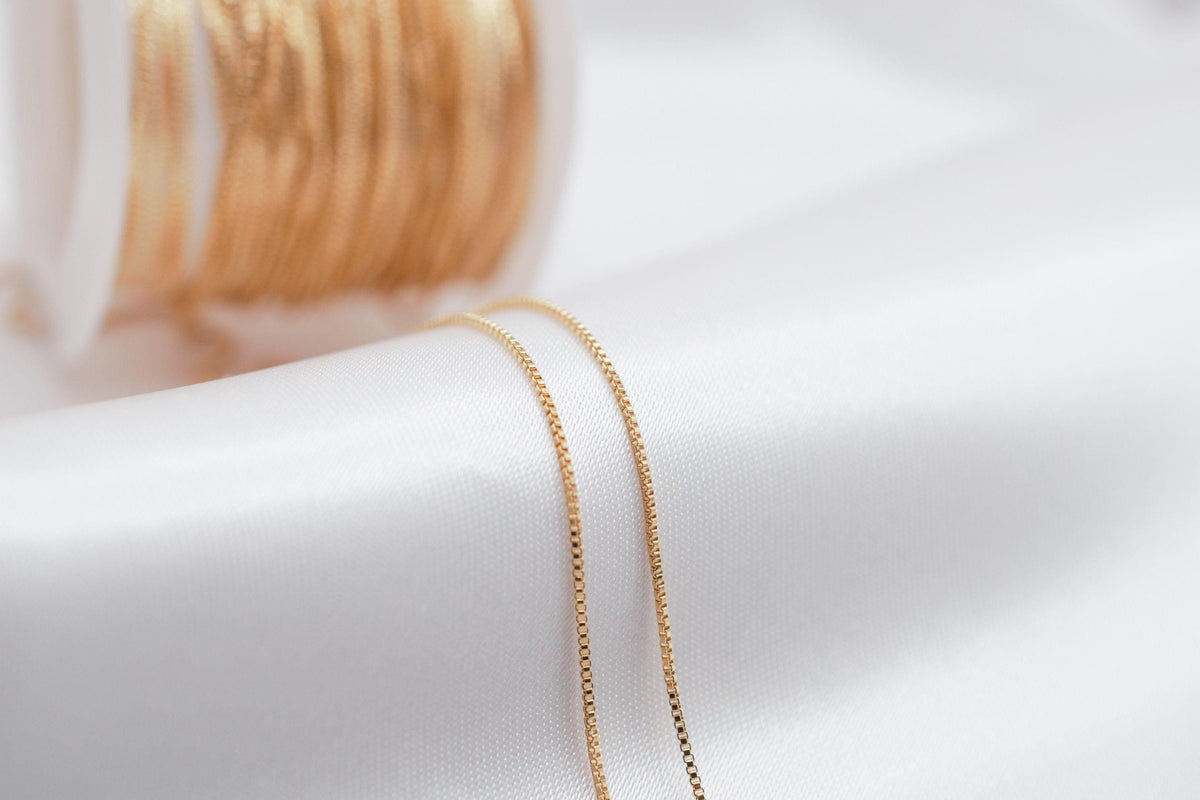 A close-up view of a gold chain necklace with a spool of gold thread visible in the background.