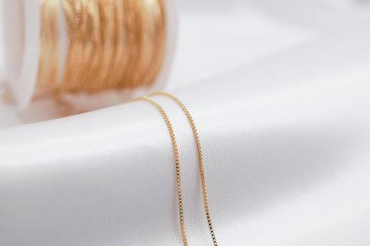 A close-up view of a gold chain necklace with a spool of gold thread visible in the background.
