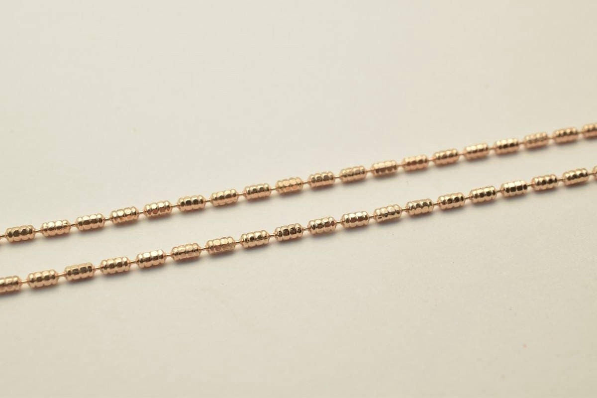A close-up image of a gold-colored chain with small, round beads arranged in a repeating pattern.