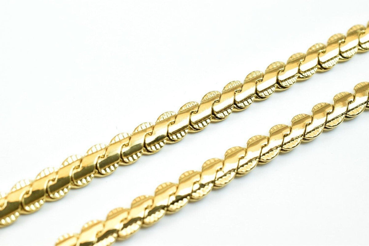A close-up view of a gold chain necklace against a white background.