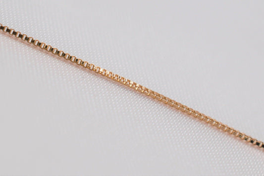 A close-up view of a gold-colored necklace chain against a white background.