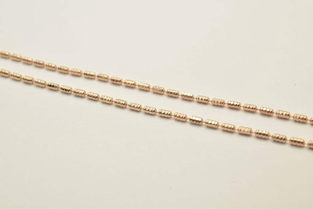 A close-up image of a gold-colored chain with small, round beads arranged in a repeating pattern.